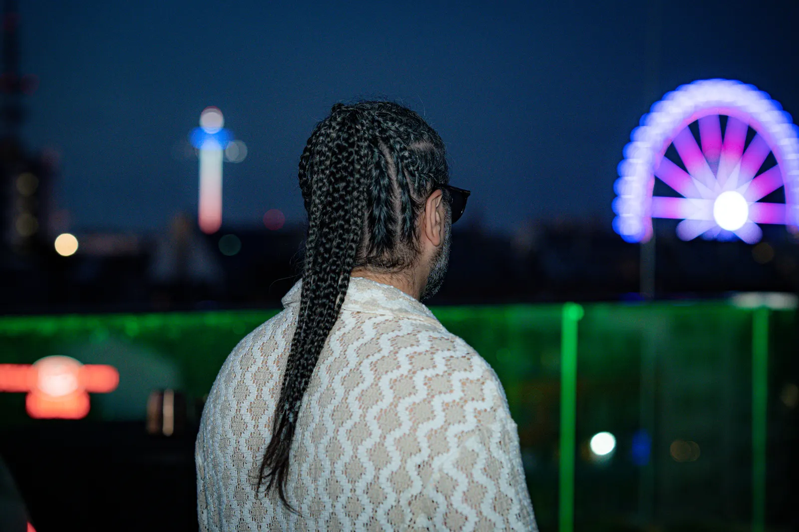 DJ Mahbod playing on a rooftop at dusk, a lit Ferris wheel behind him